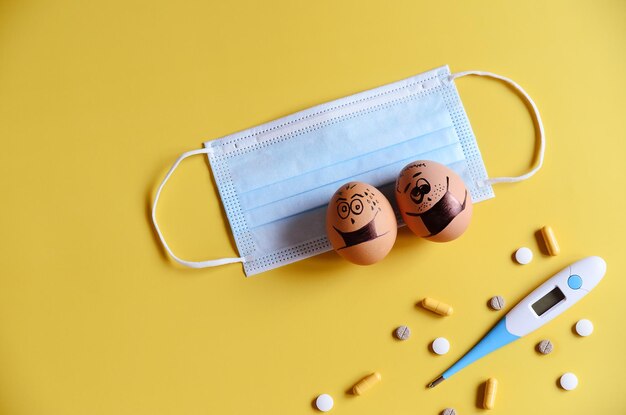 Diverse chicken eggs with doodle faces wearing medical masks on yellow background. Corona virus