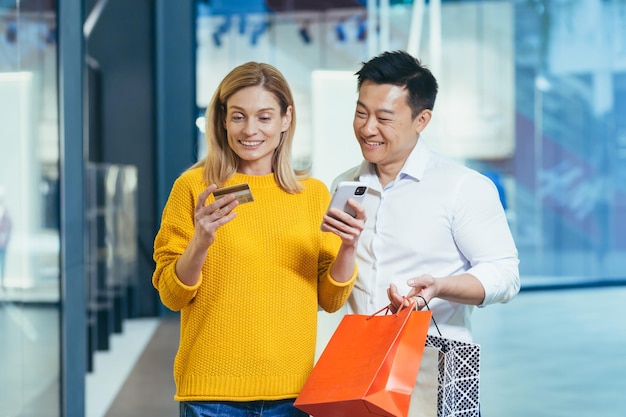 Diverse couple of shoppers asian man and woman shopping for clothes inside store smiling and happy