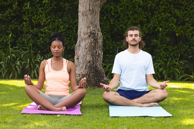 Diverse couple a young African American woman and Caucasian man meditate in a serene garden