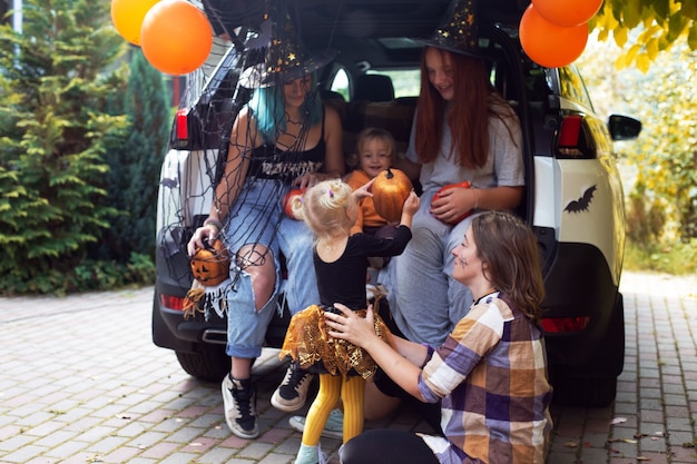 Diverse family celebrating Halloween in car trunk. Girls having fun outdoors in autumn day. High quality photo. Stay home Halloween. Celebration in isolation. Trick or treat.