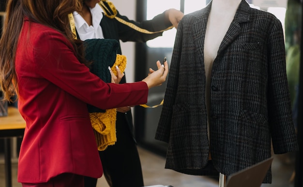 Diverse female fashion designers at work with tailor centimeters on necks and holds tablet and smartphone independent creative design business in studio