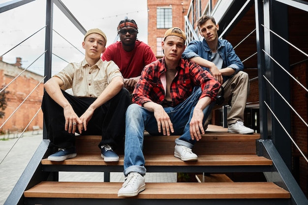 Diverse group of boys wearing street fashion while posing on metal stairs in urban setting