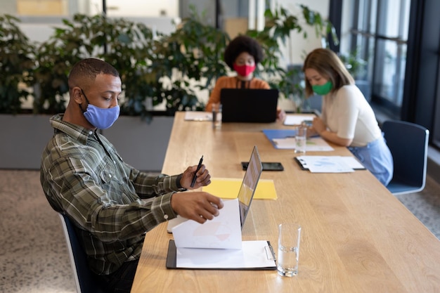 Photo diverse group of business people working in creative office. group of people wearing face masks and using laptops. social distancing protection hygiene in workplace during covid 19 pandemic.