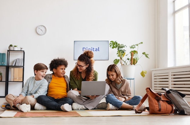 Diverse group of children sitting on floor in school with smiling female teacher