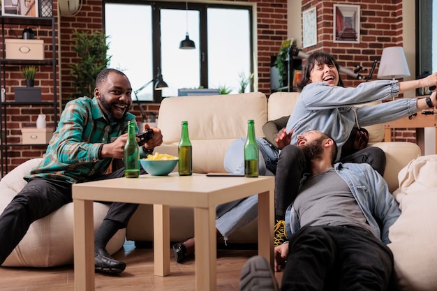 Diverse group of friends feeling happy and playing video games on television console. Smiling people having fun together with gaming competition and alcoholic beverage at gathering.