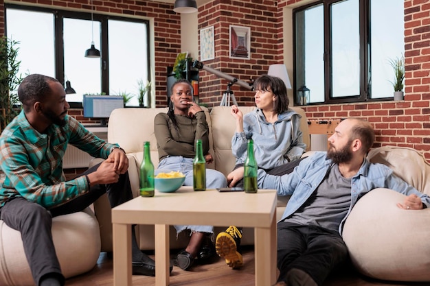 Diverse group of people having fun and laughing together at house party with beer bottles and food. Friends being happy and talking about memories, leisure activity and entertainment.