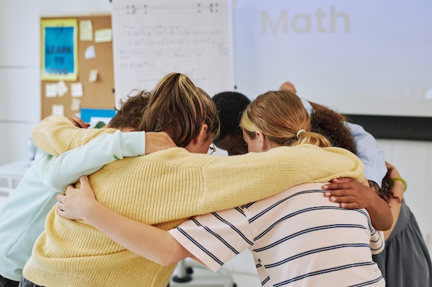 Diverse group of schoolchildren huddling in team exercise in classroom