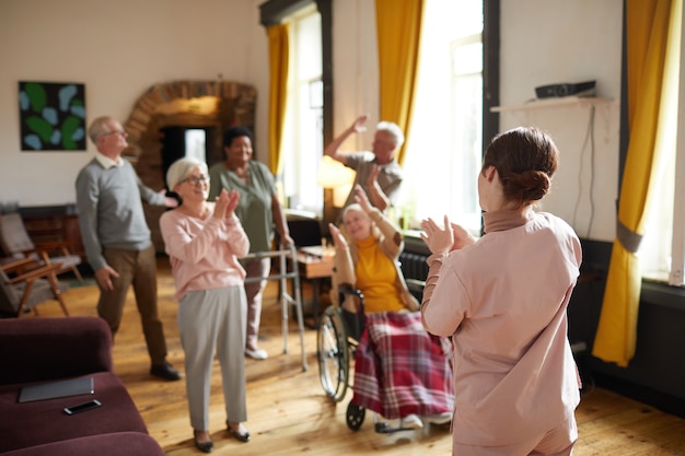 Diverse group of smiling senior people dancing while enjoying activities in retirement home with you...