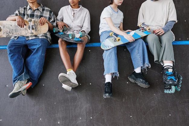 Diverse group of teenagers sitting on ramp in skateboarding park low section of feet dangling copy s