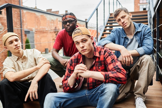 Diverse group of young guys wearing street fashion while posing on metal stairs in urban setting