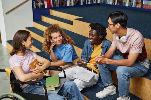 Diverse group of young people discussing work in college library including female student with disab