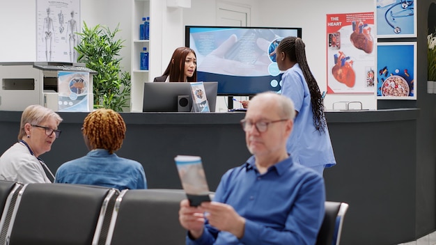 Diverse medical staff working on appointments at reception desk in hospital lobby. Nurse and receptionist helping patients with checkup visits, doing examination work at healthcare center.