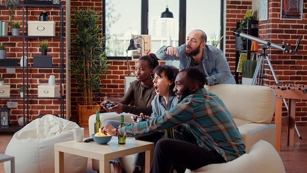 Diverse people playing video games online on console, using controller to have fun at gathering with beer bottles. Friends enjoying gaming competition on television, entertainment group.