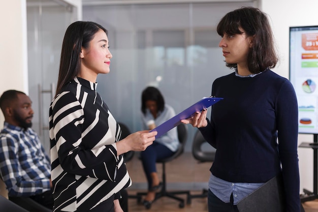 Diverse people in waiting room of startup agency talking about career oportunity and recruitment process. Asian unemployed woman giving CV resume to human resources manager in order to get interviewed