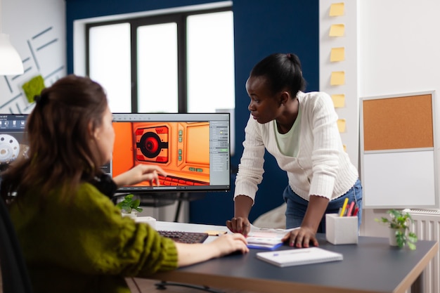 Diverse women game sofware developers testing new game sitting in startup creative agency company using pc with dual monitors setup