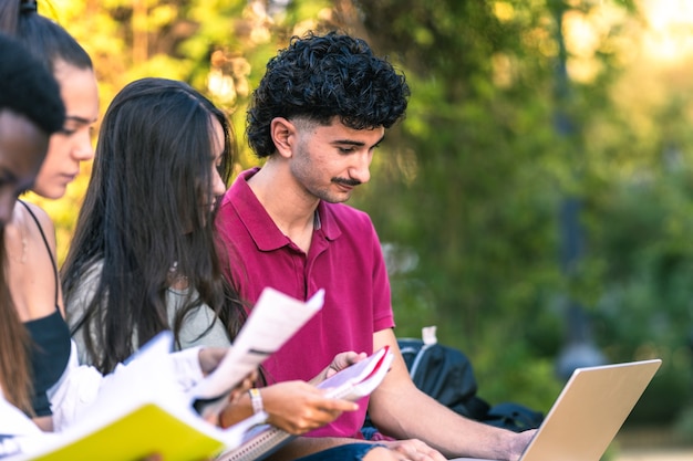 Diverse young people studying with laptop and papers sitting on a bench outdoors