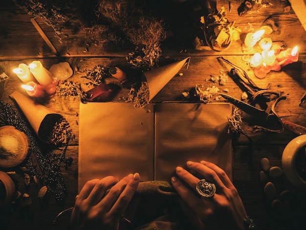 Divination with the help ancient books and of the dry African herbs. The light from the candles on the old magic table. Attributes of occultism and magic.