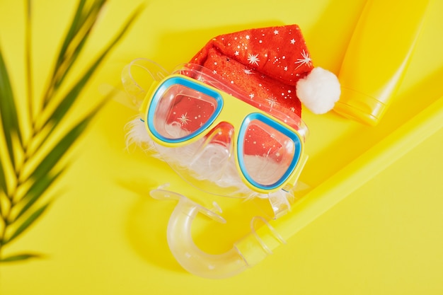 Diving set, santa claus hat and sunblock on yellow background, Christmas holidays on the beach in a warm country top view