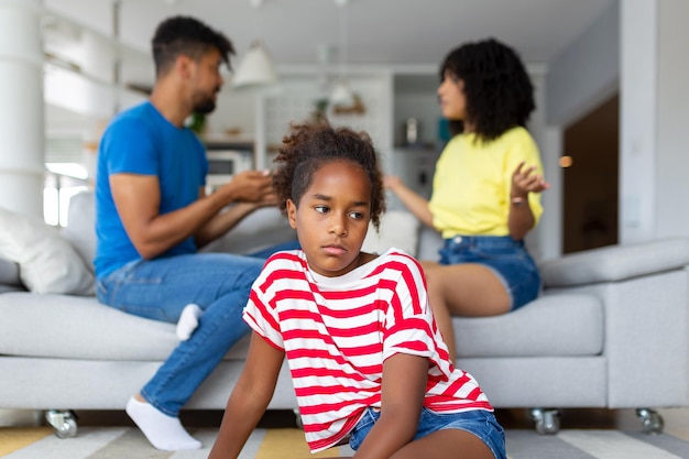 Divorce And Domestic Violence Portrait of upset African American daughter looking through the window while her angry parents fighting in the background depressed child feeling lonely