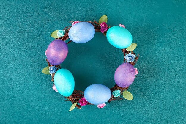 Diy Easter wreath of twigs, painted eggs and artificial flowers on a green background.