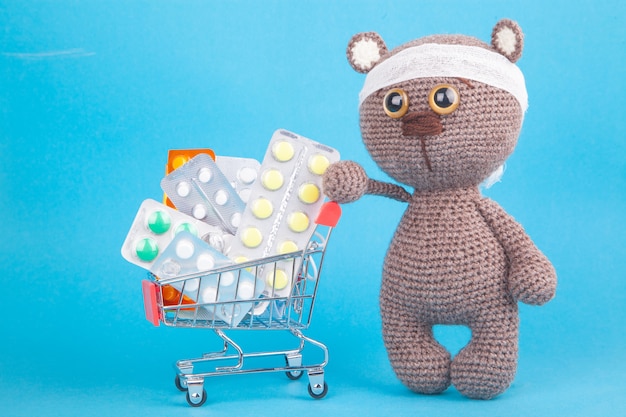 DIY toy. Knitted brown bear cub. Shopping for medicines, healthcare costs and prescription medication  with a shopping trolley filled with pills 