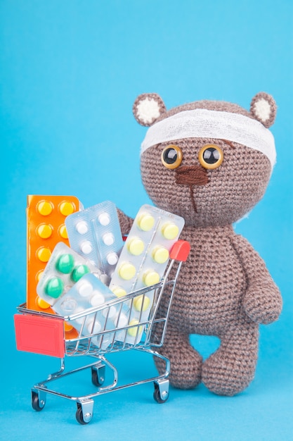 DIY toy. Knitted brown bear.  Shopping for medicines, healthcare costs and prescription medication concept with a shopping trolley filled with pills