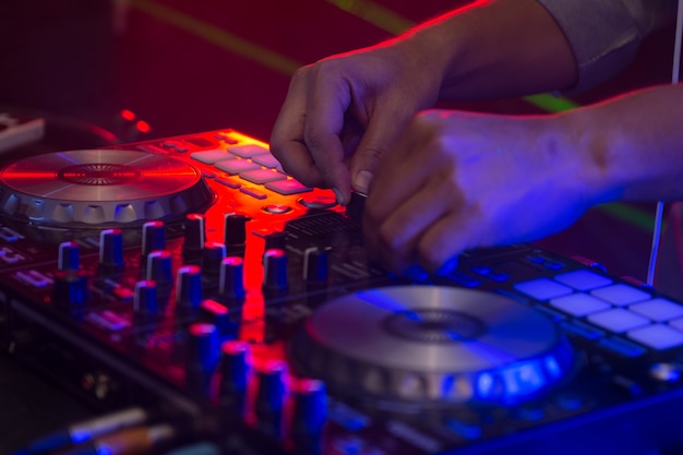 DJ hands on stage mixing, disc jockey and mix tracks on sound mixer controller, playing music at bar, disco tech or night club party.