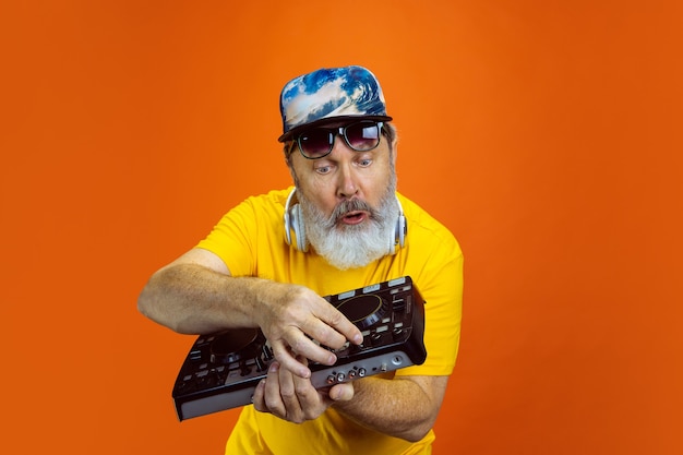 DJset Portrait of senior hipster man using devices gadgets isolated on orange studio background