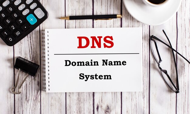 DNS Domain Name System is written in a white notepad near a calculator, coffee, glasses and a pen