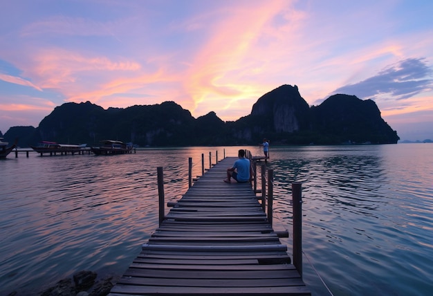 a dock with a person sitting on it and a boat in the water