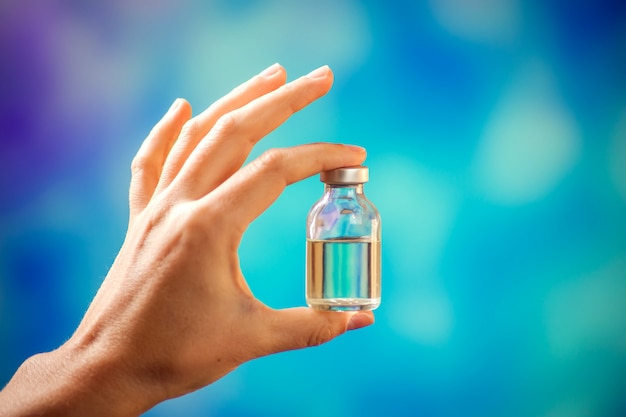 A doctor in blue gloves holding a bottle with vaccine. Close up shot. Medicine and healthcare concept