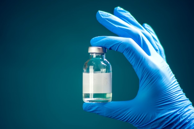 A doctor in blue gloves holding a bottle with vaccine. Close up shot. Medicine and healthcare concept