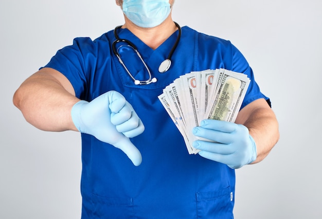 Doctor in blue uniform and latex gloves keeps one hand a lot of money, other hand shows a bad gesture