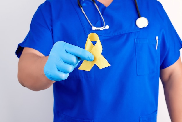 Doctor in a blue uniform and sterile latex gloves holds a yellow ribbon in his hand