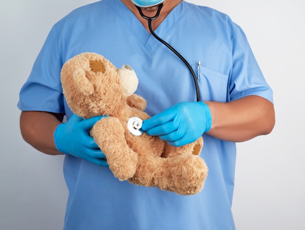 Doctor in blue uniform and white latex gloves holding a brown teddy bear, 