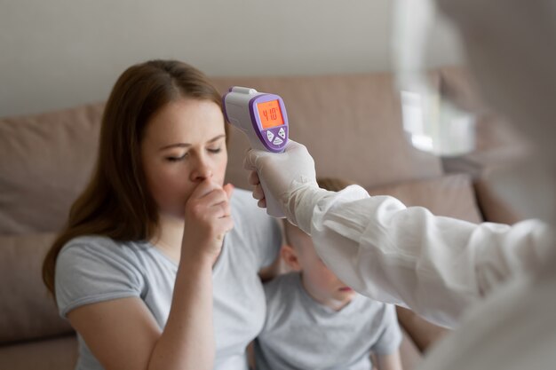 Photo doctor check patient body temperature using infrared forehead thermometer gun at home. coronavirus, covid-19, high fever and cough