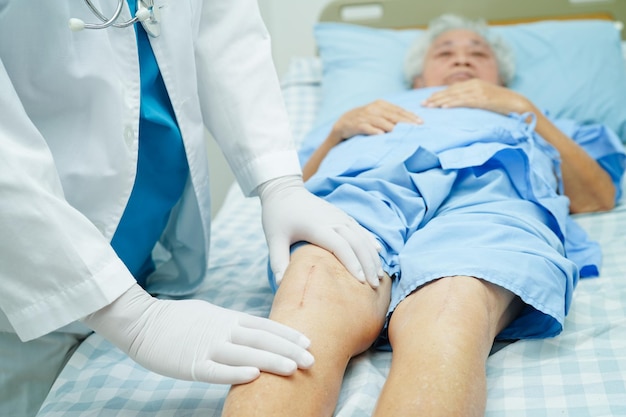 Doctor checking Asian elderly woman patient with scar knee replacement surgery in hospital