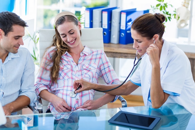 Doctor checking belly of pregnant woman with stethoscope