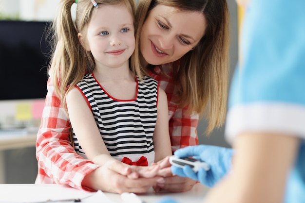 Doctor checks blood sugar level of little girl using digital glucometer at hospital