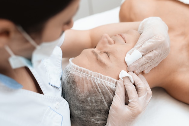 Doctor cleanses skin of man. The man is lying on the couch.