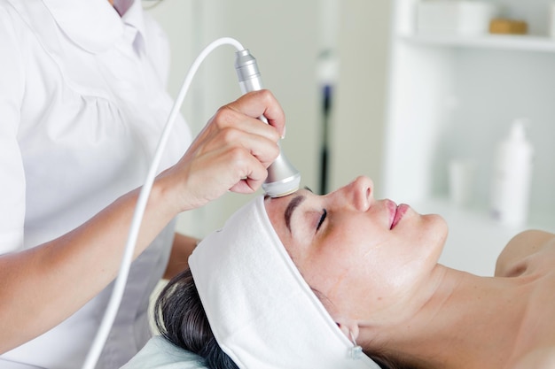 Doctor cosmetologist makes a facial procedure for a female patient with an ice cap to restore the skin