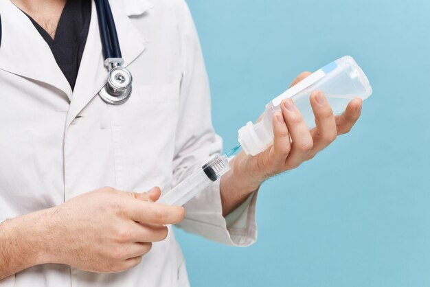 Doctor draws solution into syringe from vial in clinic office Blue background