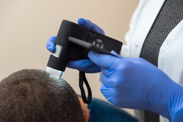 The doctor examines the patient's scalp using an optical device