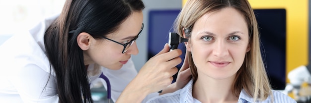 Doctor examines patients ear with an otoscope otolaryngologist services concept