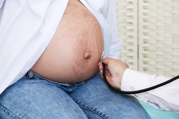 Photo doctor examines a pregnant woman by listening to the fetal heartbeat with a phonendoscope