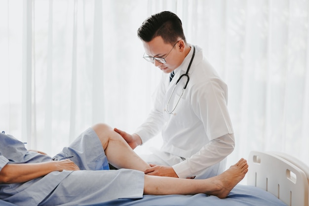 Doctor examining his patient knee on the bed in hospital