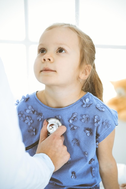 Doctor examining a little girl by stethoscope. Happy smiling child patient at usual medical inspection. Medicine and healthcare concepts.