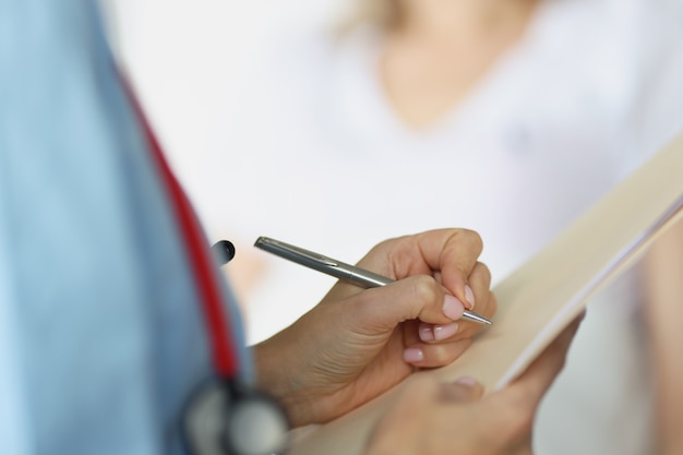 Doctor filling out patient medical documents with ballpoint pen in ward closeup. Health insurance concept