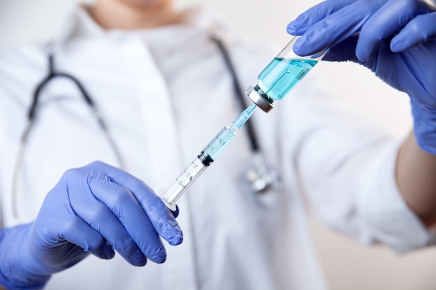 Doctor in gloves filling up syringe from bottle with vaccine medicine