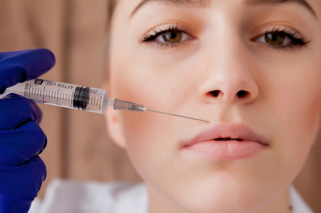 Doctor in gloves giving woman botox injections in lips, on pink background